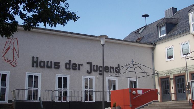 Ein Jugendzentrum mit der Aufschrift "Haus der Jugend". Das Gebäude hat einen modernen Außenbereich und ist von Bäumen umgeben.