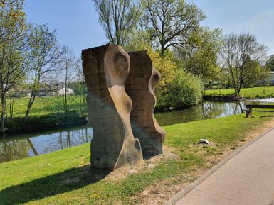 Steinskulptur am Flussufer mit Bäumen im Hintergrund.