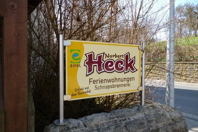 Ein Hinweisschild für Ferienwohnungen von Norbert Heck in der Eifel. Es zeigt die Informationen über die Unterkunft und die Schnapsbrennerei.