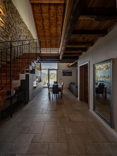 Ein modernes Wohnzimmer mit einer offenen Treppe und Holzbalkendecke. Der Raum ist hell und freundlich gestaltet, mit einem Esstisch und großen Fenstern, die auf die Aussicht blicken.