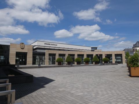 Een modern gebouw met grote ramen en een plein ervoor. De lucht is helder met enkele wolken.