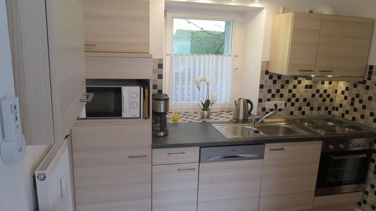 Eine moderne Küche mit hellen Holzmöbeln und einer eleganten Fliesenrückwand. Sie ist gut ausgestattet mit einem Herd, einer Mikrowelle und einem Wasserkocher.