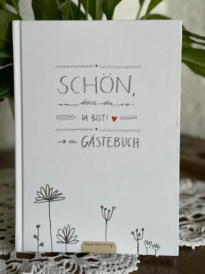 An inviting guestbook with the inscription "NICE TO HAVE YOU HERE!" and a simple drawing of flowers. It sits on a table, surrounded by decorative crochet work.