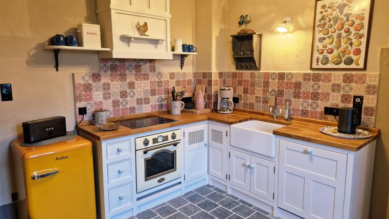 Une cuisine moderne avec un réfrigérateur jaune et un évier blanc. Les murs sont décorés de carrelages colorés, et il y a des surfaces en bois ainsi qu'une atmosphère chaleureuse.