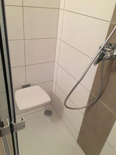 Eine moderne Duschkabine mit weißen Fliesen. Die Dusche ist kompakt und ist mit einem Handbrausekopf ausgestattet.