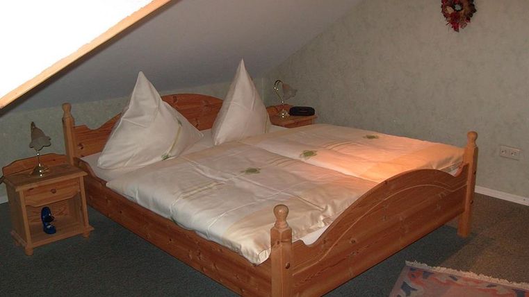 Une chambre confortable avec un lit en bois et deux coussins décoratifs. À côté du lit se trouve une table de nuit avec une lampe.