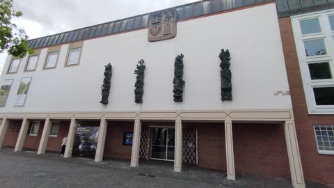 A modern building façade with sculptural elements. Above the entrance, there is a coat of arms.