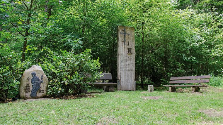 Holzdenkmal und Steinrelief im Wald mit Bänken.