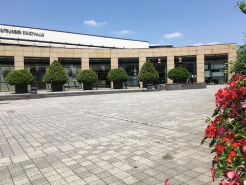 Een modern gebouw met grote ramen en onderhoudsvriendelijke planten op de voorgrond. Het plein is bestraat en biedt een uitnodigende sfeer.