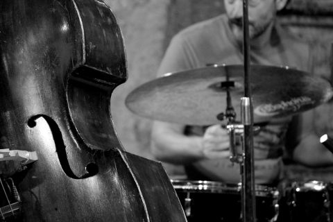A double bass stands in the foreground while a drummer plays in the background. The scene conveys a lively jazz atmosphere.