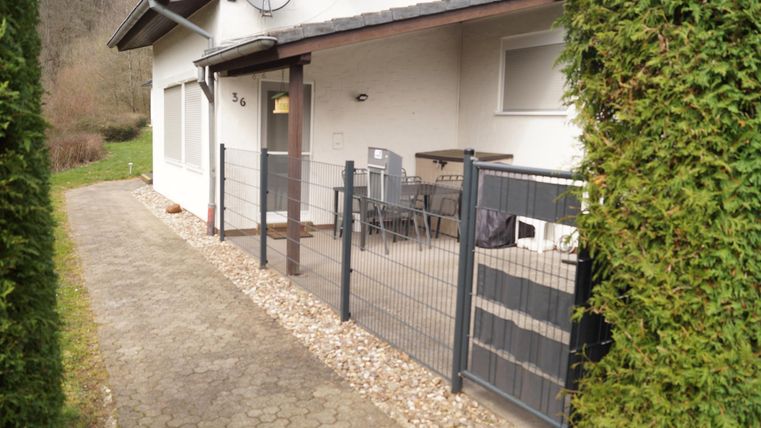 Ein modernes Haus mit einem Eingangsbereich und einem kleinen Garten. Vor dem Haus stehen Stühle und ein Tisch auf der Terrasse.