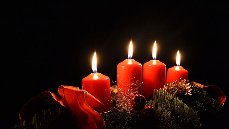 Four red candles burn brightly on a decorated table. The background is dark, which emphasizes the warm lighting atmosphere.