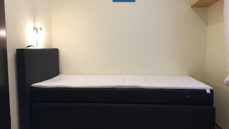 Ein einfaches Schlafzimmer mit einem schwarzen Bett und einem Wandregal. An der Wand hängt ein kleines Gemälde.