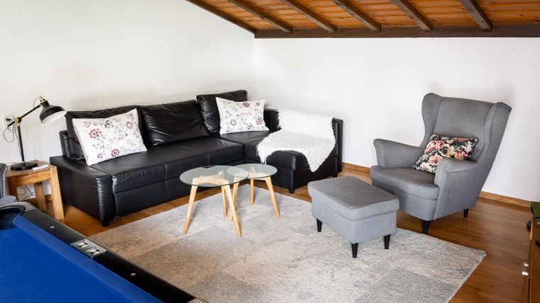 Ein gemütlicher Wohnbereich mit einer schwarzen Couch und einem grauen Sessel. Der Raum hat eine Holzdecke und einen kleinen Tisch in der Mitte.