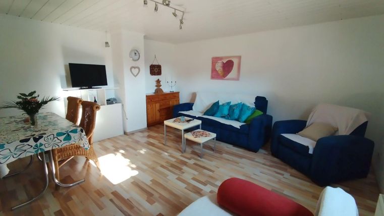 Ein helles Wohnzimmer mit modernen Möbeln. Es gibt eine Sitzecke, einen Essbereich und eine gemütliche Atmosphäre.