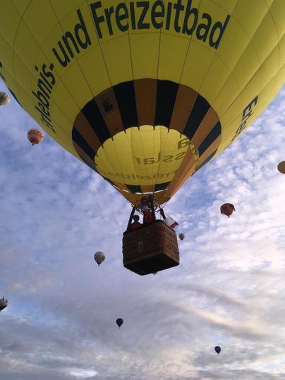 Ein heißluftballon schwebt hoch am Himmel, umgeben von mehreren anderen Ballons. Die Wolken im Hintergrund verleihen der Szene eine ruhige Atmosphäre.