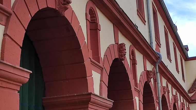 A historic building with red arches and decorative stonework. The facade showcases a combination of red and light colors.