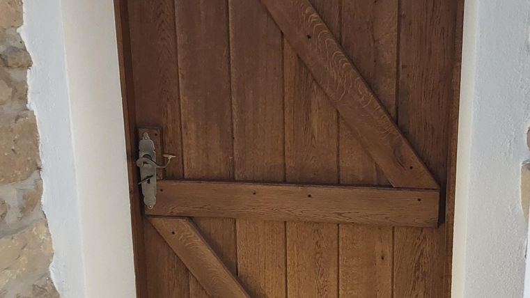 Een mooie houten deur met een diagonale steun. De deur is te zien in een moderne ruimte met tegels op de vloer.