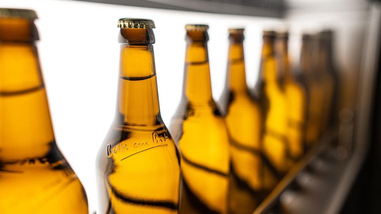 Eine Reihe von braunen Bierflaschen steht aufgereiht. Die Flaschen reflektieren das Licht und erzeugen einen attraktiven Effekt.