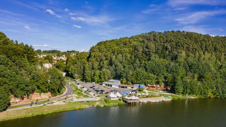 Luftaufnahme des Stausees Bitburg mit umliegendem Wald und Gebäuden.