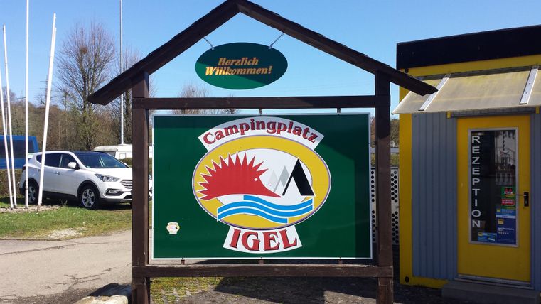 Ein Willkommensschild für den Campingplatz Igel. Das Schild zeigt Sonne, Wasser und ein Boot, um die Freizeitaktivitäten zu symbolisieren.