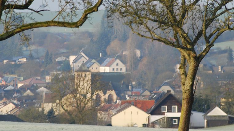Eine malerische Aussicht auf ein Dorf mit einer Kirche im Hintergrund. Die Landschaft ist von Bäumen umrahmt und zeigt ein ruhiges, ländliches Ambiente.