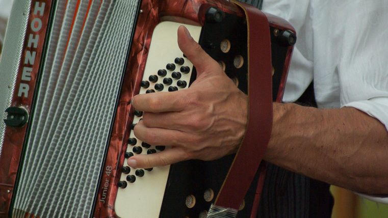 Eine Person spielt ein Akkordeon mit einer kräftigen Hand. Das Instrument hat eine markante rot-schwarze Färbung.