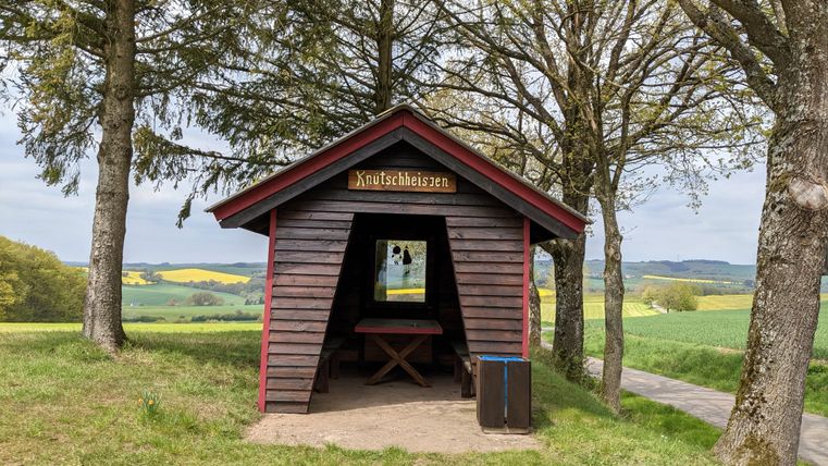 Holzhütte mit Schild 'Knutschheisjen' in ländlicher Umgebung.