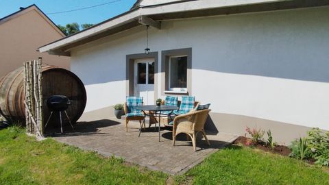 Eine gemütliche Terrasse mit einem Tisch und Stühlen. Im Hintergrund steht ein großes Holzfass und ein Grill.