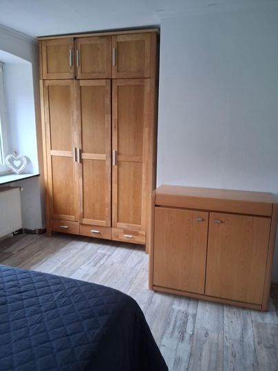 Ein schlichtes Schlafzimmer mit einem großen Holzschrank und einem kleinen Holzschrank. Der Boden ist hell und die Wände sind neutral gehalten.