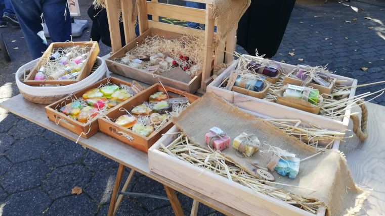 A table with various handmade soaps in wooden boxes. The soaps are colorful and attractively arranged, surrounded by straw.
