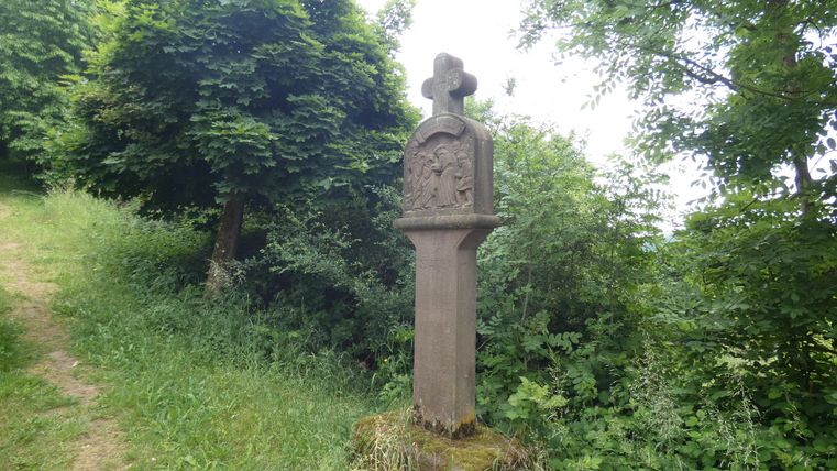 Monument de chemin de croix en pierre dans un paysage forestier verdoyant.