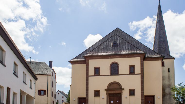 Pfarrkirche St. Peter in Neidenbach mit spitzem Kirchturm und umliegenden Gebäuden.