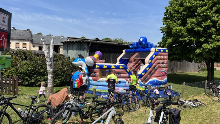 Une aire de jeux colorée est installée dans un jardin vert, entourée de vélos. Les enfants s'amusent à jouer.