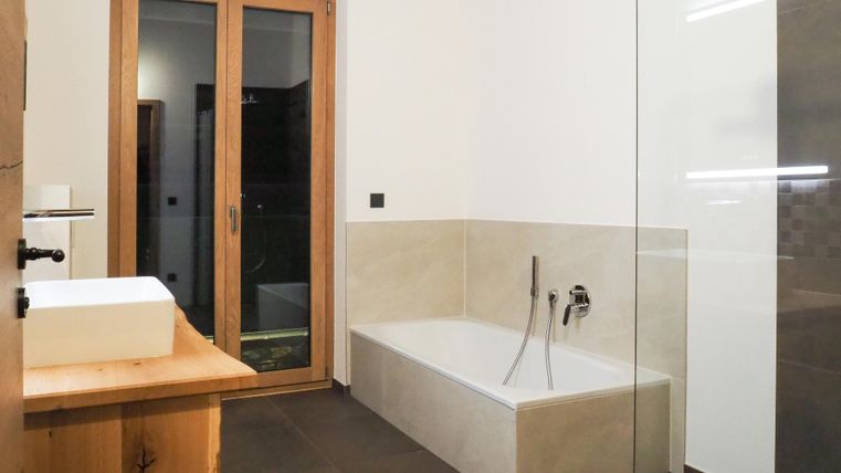 Ein modernes Badezimmer mit einer Badewanne und einem Waschbecken aus Holz. Große Glastüren sorgen für viel Licht und eine offene Atmosphäre.
