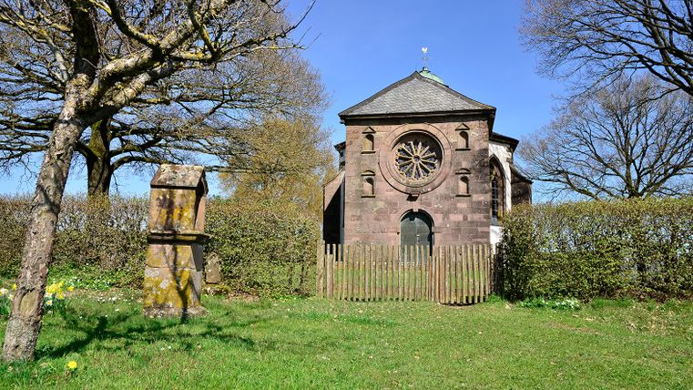 Frohnertkapelle in Oberkail mit Bäumen und einem alten Grabstein im Vordergrund.