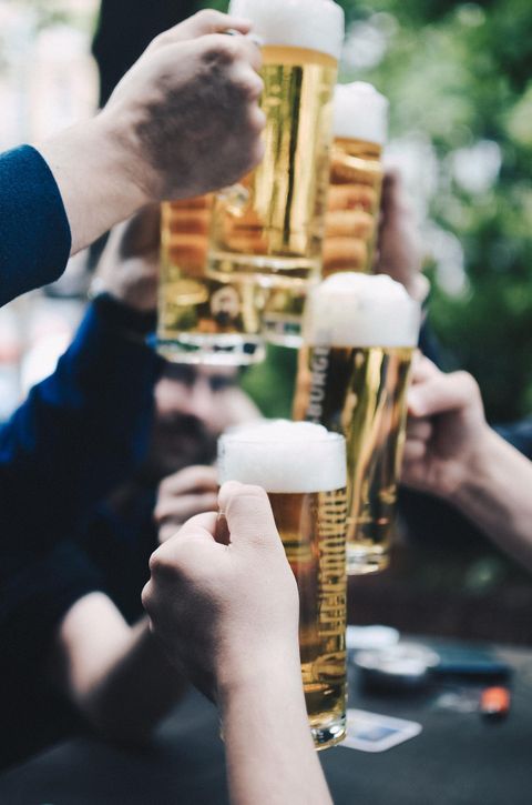 A group of people clinks beer glasses together. The glasses contain pale beer and have a frothy top.