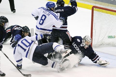 An exciting ice hockey game with players battling for the puck. The goalie is trying to prevent a goal while one player has fallen to the ground.