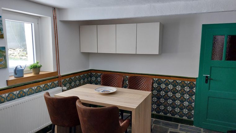 Een gezellige eetruimte met een houten tafel en bruine stoelen. De muren zijn kleurrijk ingericht, en een groene deur voegt een accent toe.