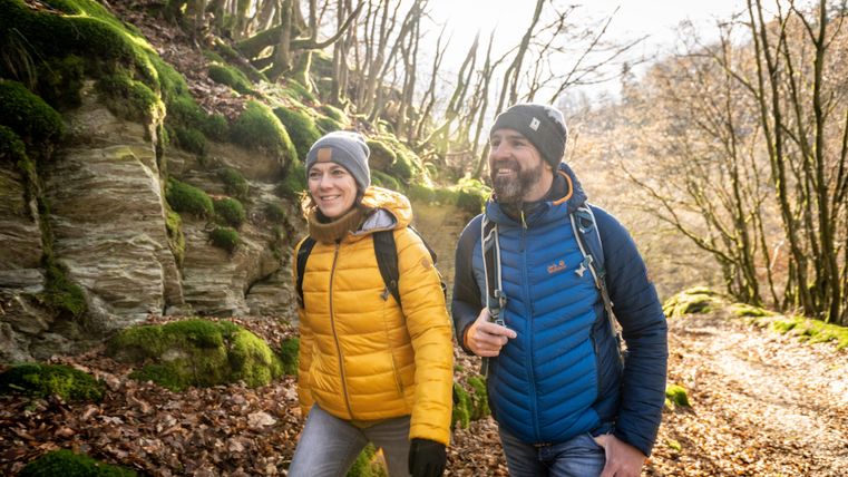 Deux randonneurs sur un joli sentier forestier avec de la mousse verte et des rochers. Il semble qu'il fasse un jour ensoleillé et la nature autour d'eux est vivante.