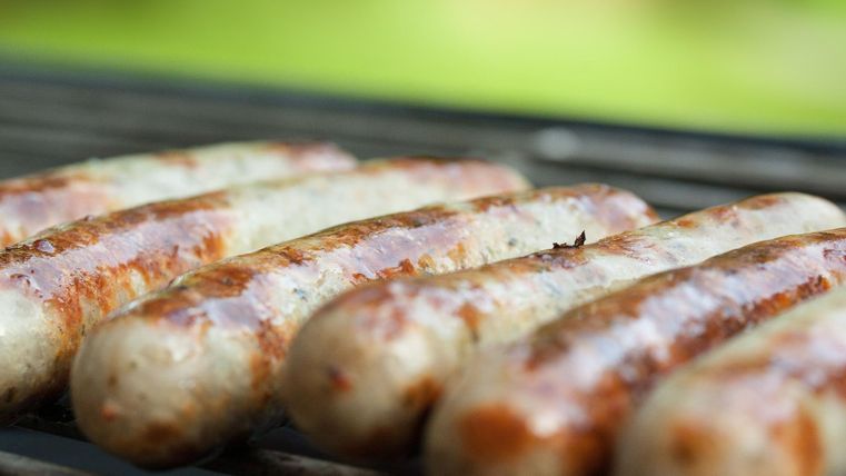Grilled sausages are lying on a grill. They are browned and golden brown, surrounded by a blurred green background.