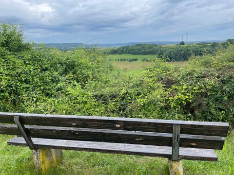 Eine Holzbank steht vor einer grünen Landschaft mit bewölktem Himmel.