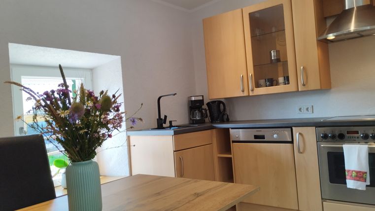 Eine moderne Küche mit Holzmöbeln und einer schönen Blumenvasen auf dem Tisch. Im Hintergrund sind Fenster, die natürliches Licht hereinlassen.