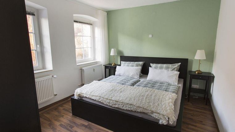 Ein modernes Schlafzimmer mit einem Doppelbett und zwei Nachttischen. Die Wände sind in einer sanften Farbgebung gehalten, und es gibt große Fenster, die viel Licht hereinlassen.