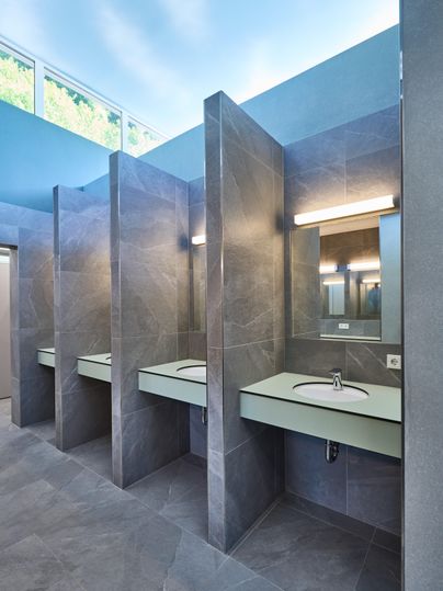 Ein modernes Badezimmer mit grauen Fliesen und eleganten Waschbecken. Die Räume sind hell und gut beleuchtet.