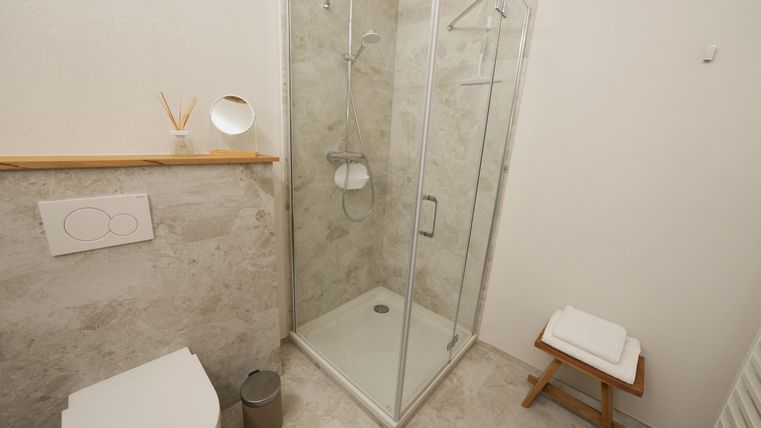Een moderne badkamer met een douchecabine, een toilet en een houten planken. Witte tegels en een lichte, schone sfeer creëren een aangename ambiance.