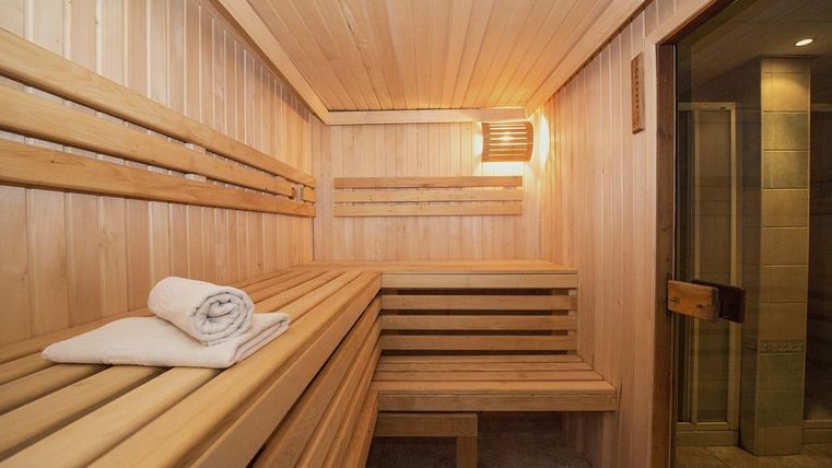 Een heldere sauna met houten banken en zachte verlichting. Een vers handdoek ligt klaar.
