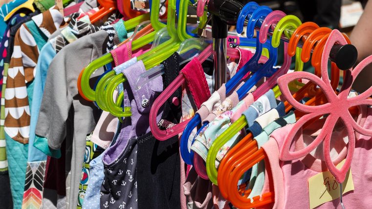 Bunte Kinderkleidung, die an einem Stand hängt. Die Kleider sind an leuchtenden Bügeln befestigt.