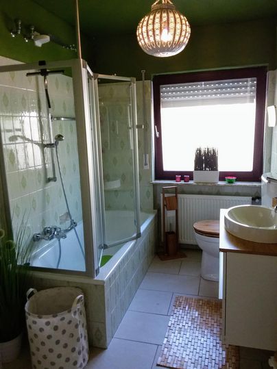 Une salle de bain moderne avec une douche et une baignoire. La pièce a des murs verts et une grande fenêtre laissant entrer la lumière naturelle.