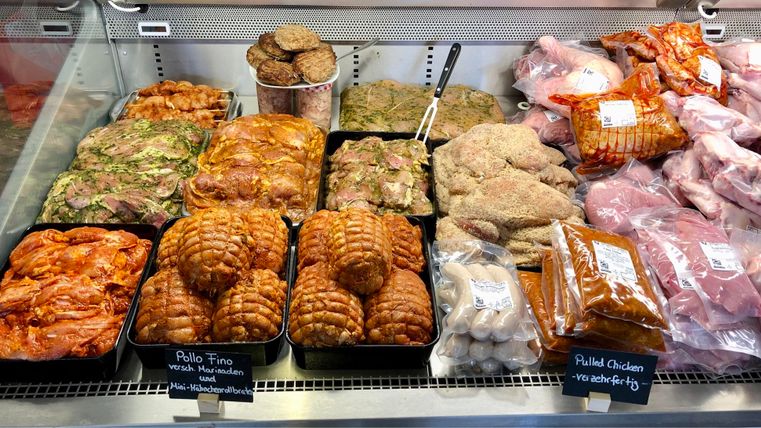 Frische Fleischwaren in einer Fleischerei. Auf der Theke sind verschiedene Fleischsorten und mariniertes Fleisch aufgereiht.